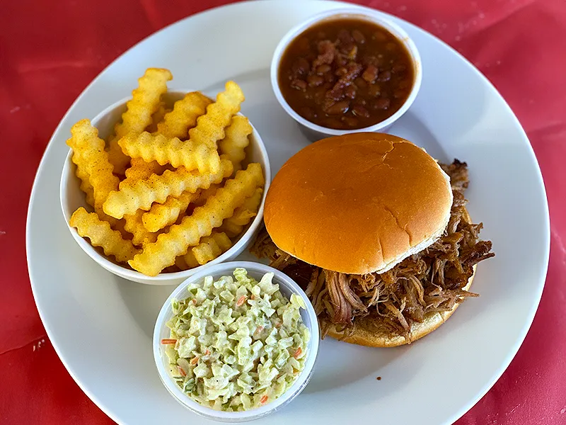 Pulled pork sandwich with crinkle fries, baked beans, and coleslaw on a white plate
